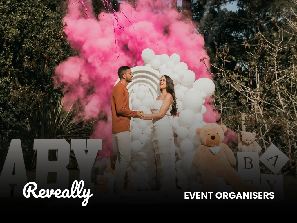 A couple at a gender-reveal celebration amid pink smoke and balloons